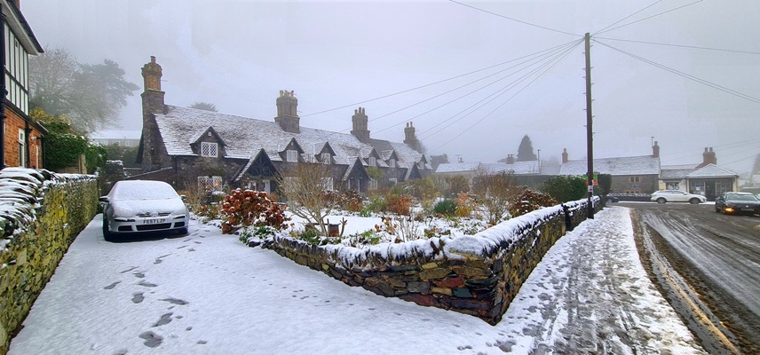 a snow covered garden, driveway, and stone wall